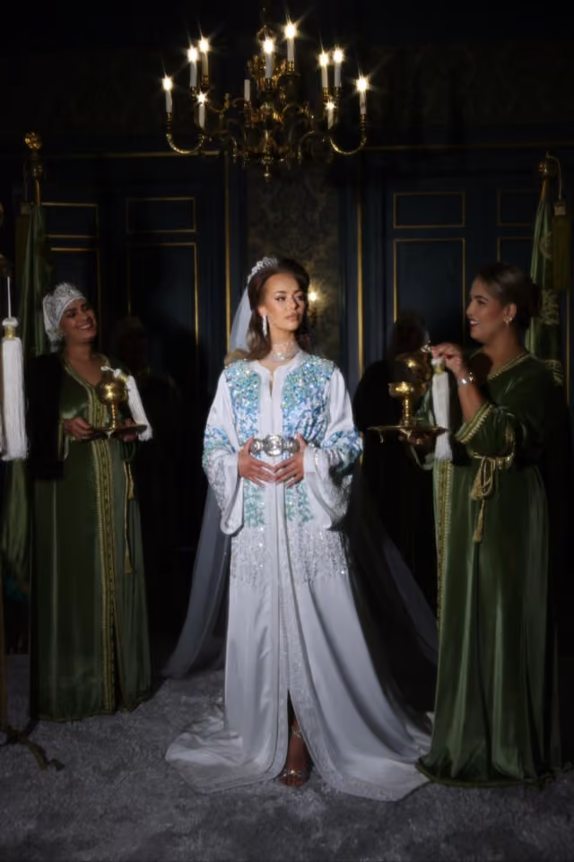 Witte kaftan met blauwe accenten onder een gouden kroonluchter